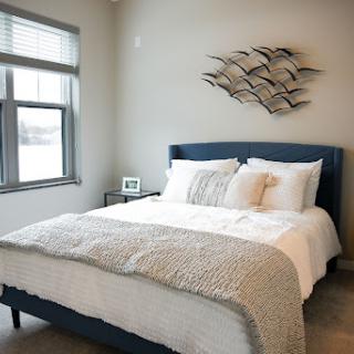 A cozy and modern bedroom featuring a neatly made bed, decorative pillows, and an artistic wall piece.
