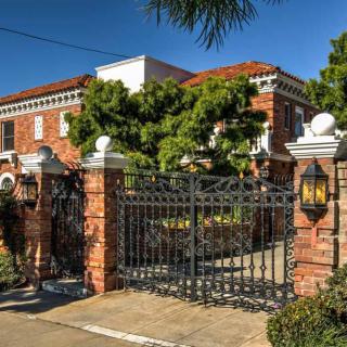 A large brick mansion with an ornate metal gate and surrounding greenery.