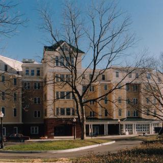 A mid-rise residential building with bare trees in front, under a clear blue sky.
