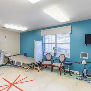 A rehabilitation room with exercise equipment and seating in a medical facility.