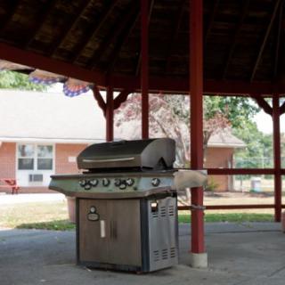 A barbecue grill placed under a gazebo in a park setting.