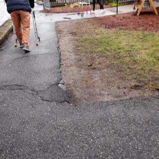 An elderly person using a walker on a pathway near a playground.