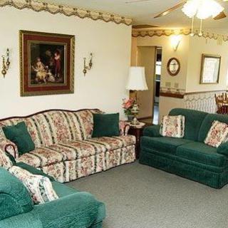 A cozy living room with floral-patterned and green sofas, a decorative painting on the wall, and a standing lamp.