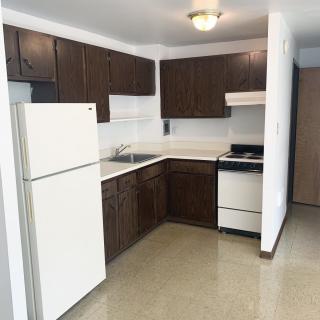 A simple apartment kitchen with dark wooden cabinets, a white fridge, and a stove.