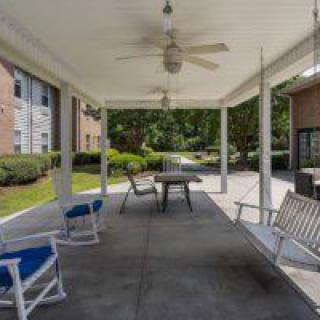 A covered patio with rocking chairs and a table at an apartment complex.