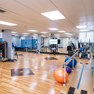 A spacious gym with various fitness equipment, wooden floors, and large mirrors.