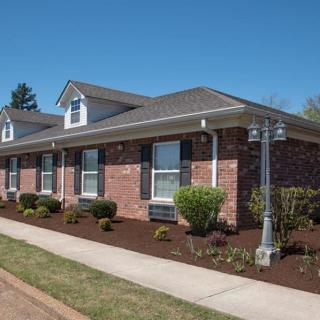 A well-maintained brick house with a landscaped front yard and sidewalk, featuring a lamp post.