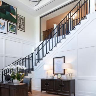 A modern interior featuring a grand staircase adorned with wall art and a stylish console table with lamps and decor.