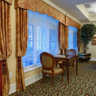 A warmly decorated room with elegant curtains, a patterned carpet, and a small table with chairs by the window.