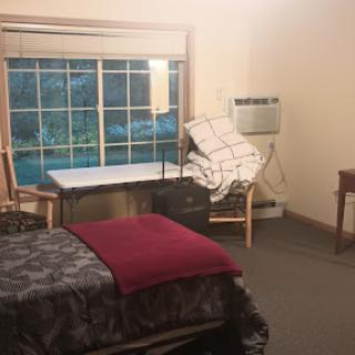 A cozy bedroom featuring a neatly made bed, a desk, and a window with a view.