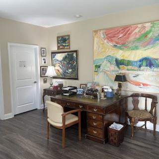 A cozy office space featuring a wooden desk, comfortable chairs, and colorful artwork on the wall.