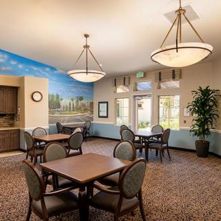 A well-lit dining area with tables and chairs, featuring a decorative mural and indoor plants.