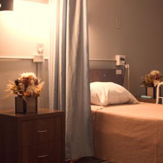 A serene hospital patient room featuring a neatly made bed and decorative flowers on the bedside table.
