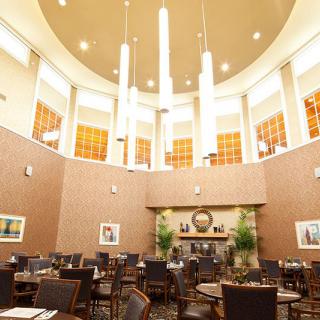 A modern restaurant interior with a high ceiling and elegant chandelier, featuring neatly arranged tables and chairs.
