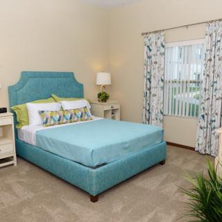 A cozy and well-decorated bedroom featuring a teal bed and matching headboard, complemented by patterned curtains and a bedside lamp.