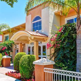 A sunny day view of a well-maintained building entrance, surrounded by lush greenery and colorful flowers.