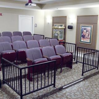 A cozy home theater setup with multiple rows of seating, a projector, and movie posters on the walls.