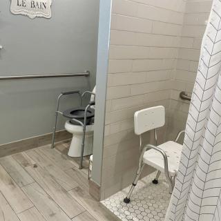 An accessible bathroom featuring a toilet and a shower with a shower chair and safety grab bars.