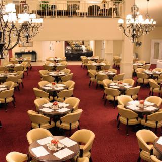 A spacious and elegantly designed restaurant dining area with chandeliers and neatly arranged tables and chairs on a red carpet.