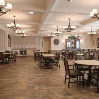 An empty dining area with multiple tables and chairs, featuring chandeliers and a wooden floor.