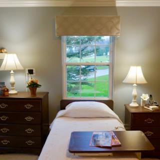 A cozy bedroom featuring a single bed, wooden nightstands with lamps, and a bright window view.