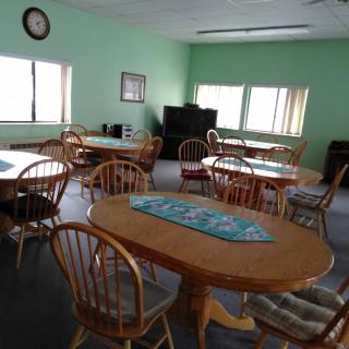 A communal dining area with multiple tables and chairs, featuring a television and natural light from the windows.