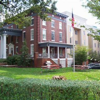 A brick residential building with a porch and an American flag on the lawn.