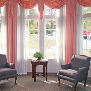 A cozy sitting area with two armchairs and a table by the window, adorned with pink curtains.