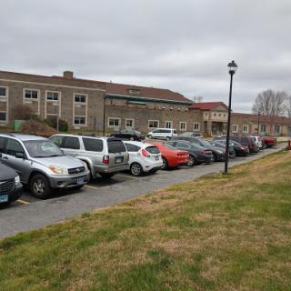 A view of a parking lot with various cars parked alongside a building, set against a cloudy sky.