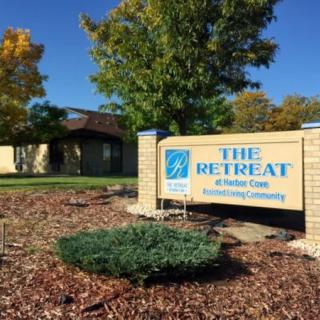 Sign for The Retreat residential community with a background of trees and buildings.