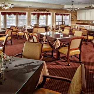 An empty dining room with neatly arranged tables and chairs, featuring large windows and elegant decor.