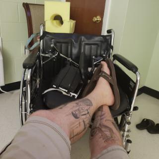 A casual moment with a focus on the legs adorned with tattoos, set against a backdrop including a wheelchair.