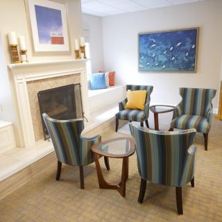 A cozy living room with striped chairs arranged around a small table, featuring a fireplace and colorful artwork on the walls.