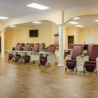 A spacious waiting area with multiple recliner chairs arranged in rows and a television mounted on the wall.