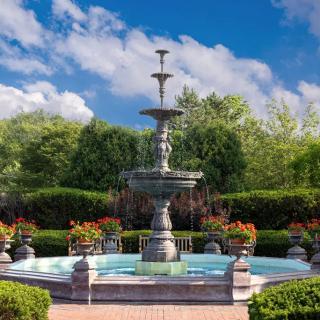 A decorative garden fountain surrounded by lush greenery and vibrant flowers under a clear blue sky.