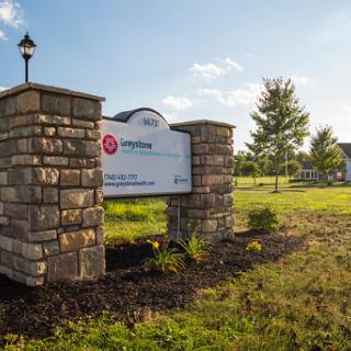 A well-maintained sign marking the entrance to a community or park, surrounded by lush landscaping and bathed in sunlight.