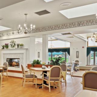 A cozy dining area with a fireplace, surrounded by tables and chairs, featuring natural light from large windows.