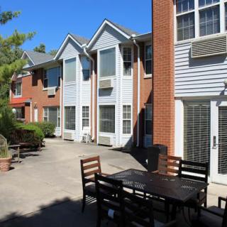 A sunny courtyard surrounded by residential apartments, featuring outdoor seating and a clear blue sky.