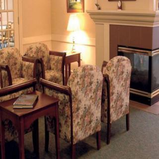 A cozy living room with floral chairs arranged around a wooden table beside a fireplace.