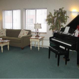 A cozy living room with a piano, sofa, and a lamp near large windows.
