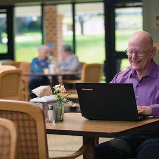 A senior individual using a laptop in a comfortable cafe environment.