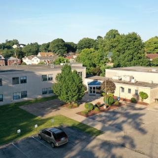 Aerial view of a modern building surrounded by greenery and a parking lot.