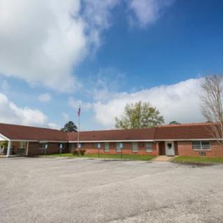 A single-story brick motel with a parking lot and cloudy sky.