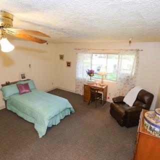 A cozy bedroom with a single bed, armchair, desk, and ceiling fan.