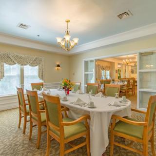An elegantly decorated dining room with a set table and comfortable chairs, featuring soft lighting and large windows.