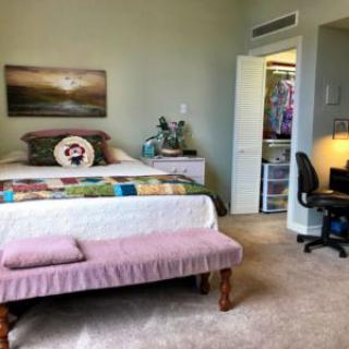 A cozy bedroom featuring a bed with a colorful quilt, an open closet, and a small desk with a chair.