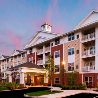 A modern apartment building with multiple floors and balconies, set against a sunset sky.