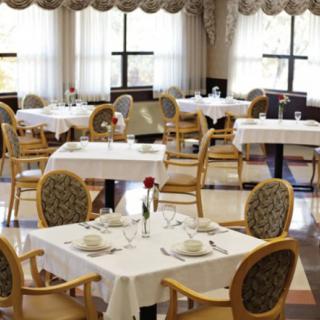 An elegant dining area with neatly arranged tables and chairs, featuring white tablecloths and large windows.