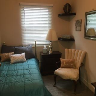 A cozy bedroom with a bed, upholstered chair, and a side table with a lamp.