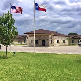 A scenic view of a building with American and Texas flags flying in front, set against a cloudy sky.